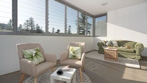 A modern living room with two armchairs, a sofa, and a coffee table. Large windows offer a view of trees and a building. - Blue Horizon on Manning (Kiama)