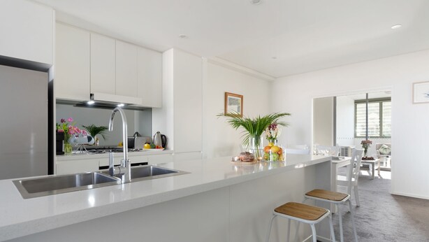 A modern kitchen with white cabinetry, stainless steel appliances, and a central island with stools. - Blue Horizon on Manning (Kiama)