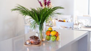A modern kitchen with a white countertop, a glass vase with green foliage, a fruit bowl, a loaf of bread, and a candle. - Blue Horizon on Manning (Kiama)