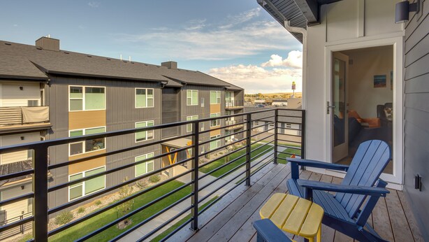 A balcony with a blue chair and a small table, overlooking a residential area with multiple buildings. - Modern Livingston Condo Near Yellowstone River! (Livingston)