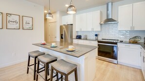 A modern kitchen with white cabinets, stainless steel appliances, and a central island with bar stools. - Modern Livingston Condo Near Yellowstone River! (Livingston)