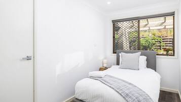 A bedroom with a bed, a nightstand, a window with a view of greenery, and a door.