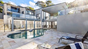A modern multi-story building with a swimming pool, outdoor seating, and a view of the surrounding area. - Coastal Breezes – water views, swimming pool, walk to beach (Corlette)