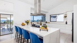 Una cucina moderna con un'isola grande, sgabelli da bar blu, vista sul mare e un'ampia finestra.