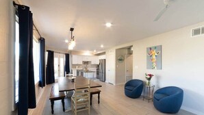 Una cocina moderna con armarios blancos, una mesa de comedor con sillas y una silla azul junto a la ventana.
