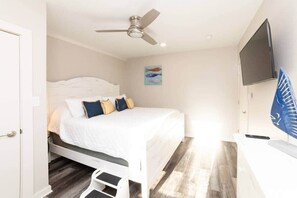Une chambre à coucher avec un lit, un ventilateur de plafond, une télévision et des œuvres d’art accrochées au mur.