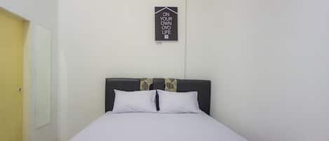 A neatly made bed with white bedding in a room with a plain white wall and a door to the left.