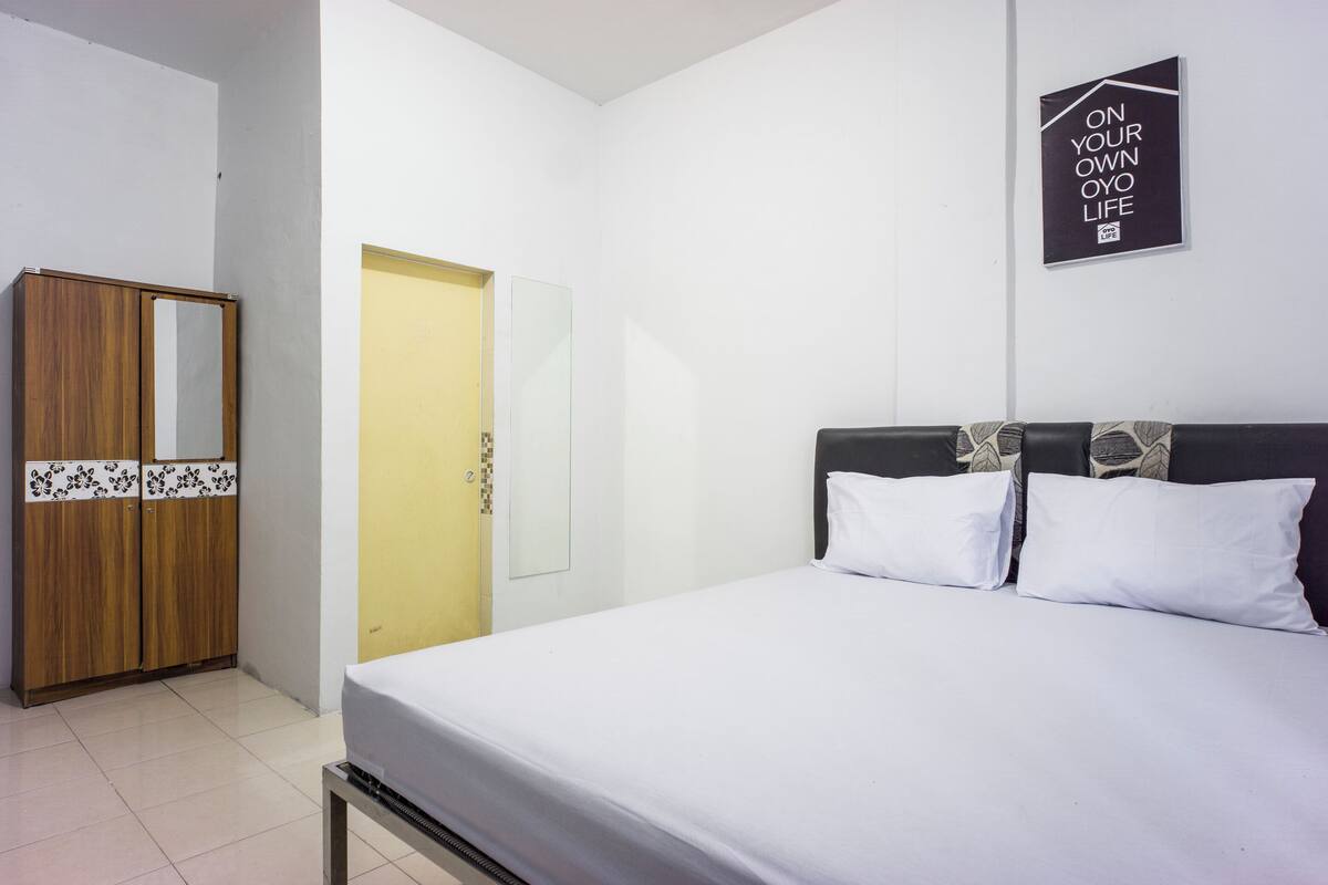 Hotellihuone, jossa on sänky, vaatekaappi, peili ja ovi.