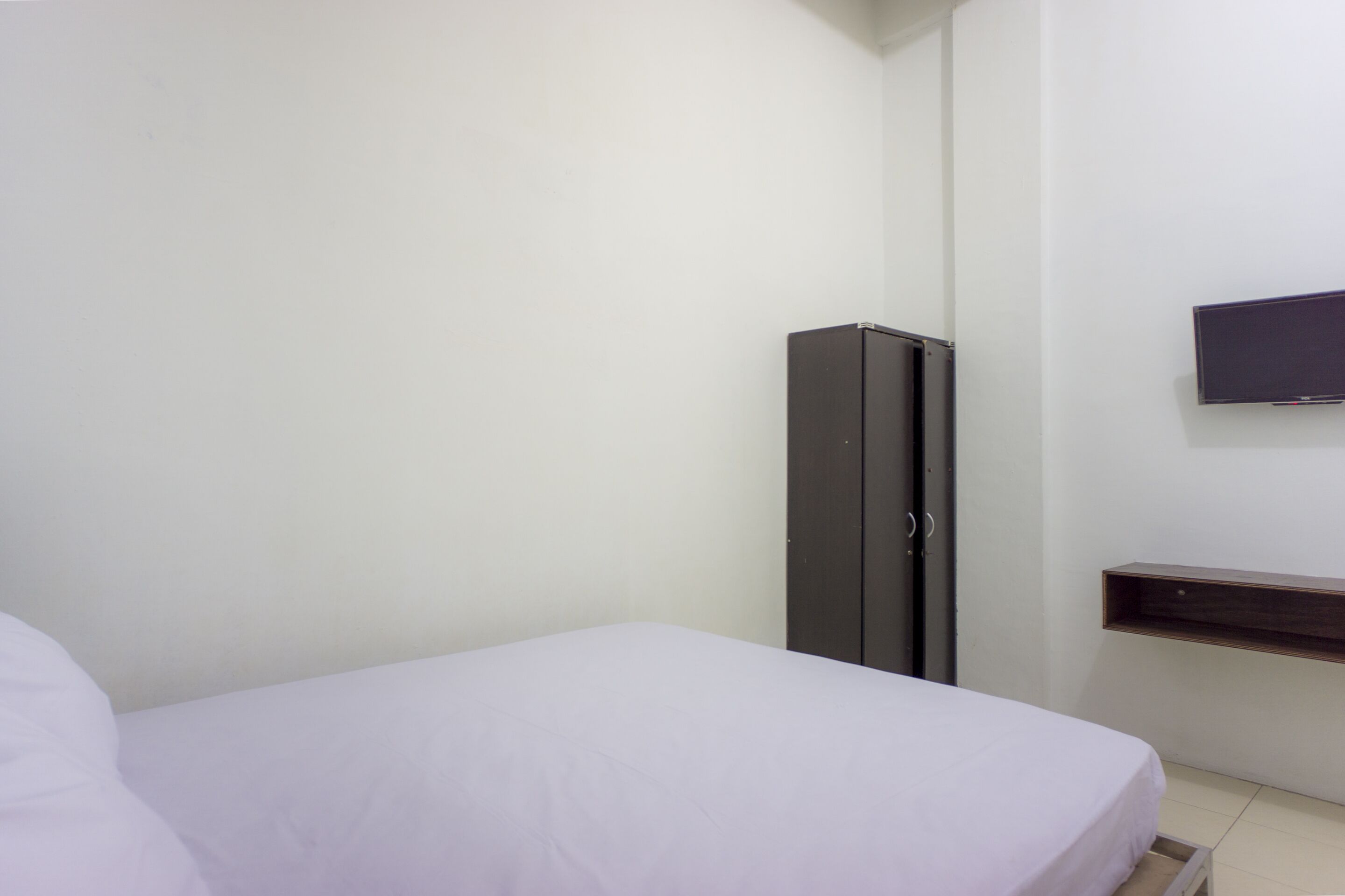 Un dormitorio con cama, armario y televisor montado en la pared.