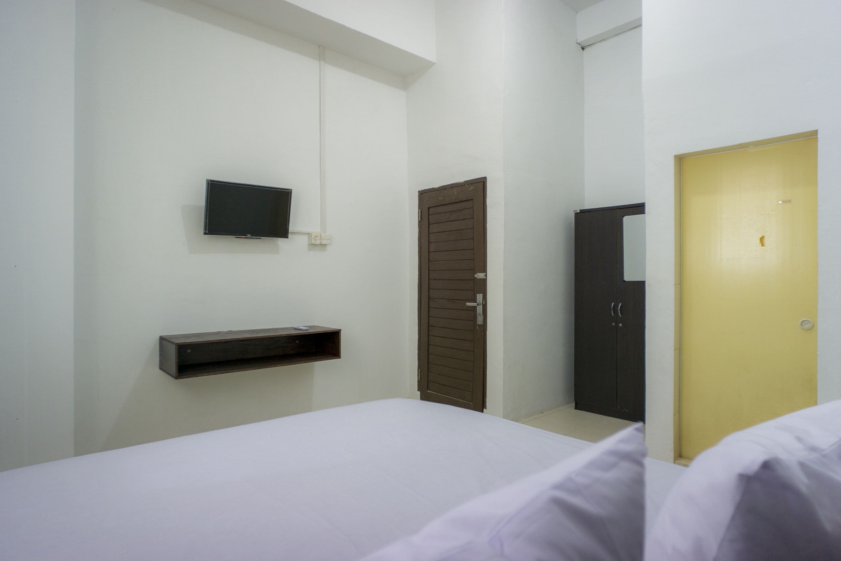 Een hotelkamer met een bed, een aan de muur bevestigde televisie, een kledingkast en een deur.