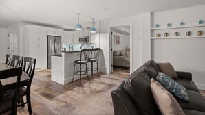 A modern kitchen with white cabinets, a central island with bar stools, a dining area with a dark wooden table and chairs, and a living room with a leather couch and decorative pillows. - Tranquil Farmhouse Condo w/ Hot Tub + Dog-Friendly (Warren)