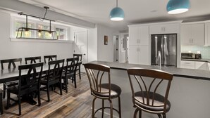 A modern kitchen with white cabinets, a stainless steel refrigerator, and a dining area with wooden chairs and a table. - Tranquil Farmhouse Condo w/ Hot Tub + Dog-Friendly (Warren)