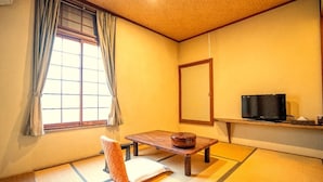 A traditional Japanese room with tatami flooring, a low table with a bowl, a chair, a television, and a sliding door. - Hotel Sumire (Shimonoseki)