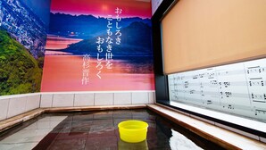 A room with a large mural of a sunset over a body of water, a piano with sheet music, and a yellow bucket on the floor. - Hotel Sumire (Shimonoseki)