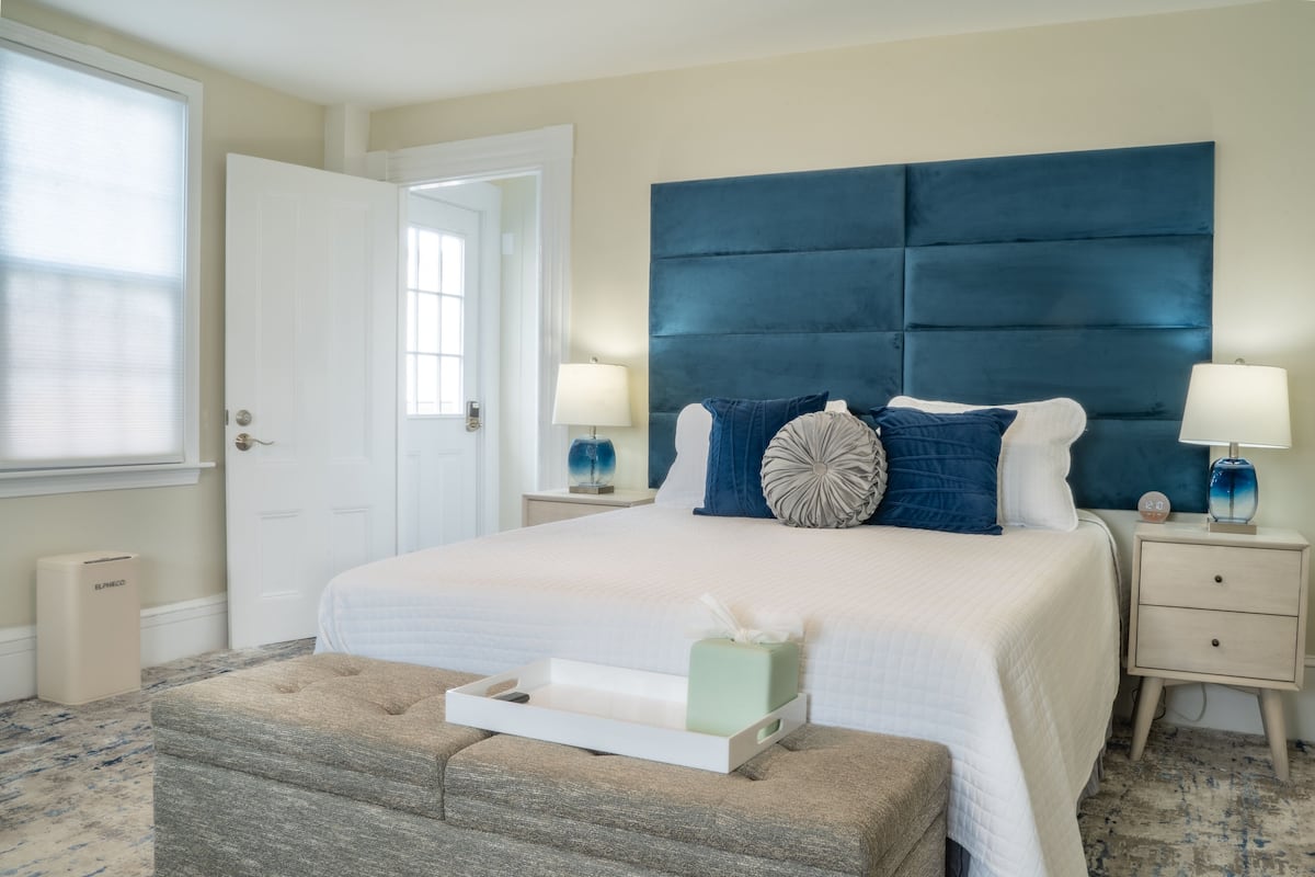 A bedroom with a large bed, two bedside tables, a nightstand, a window, and a door.