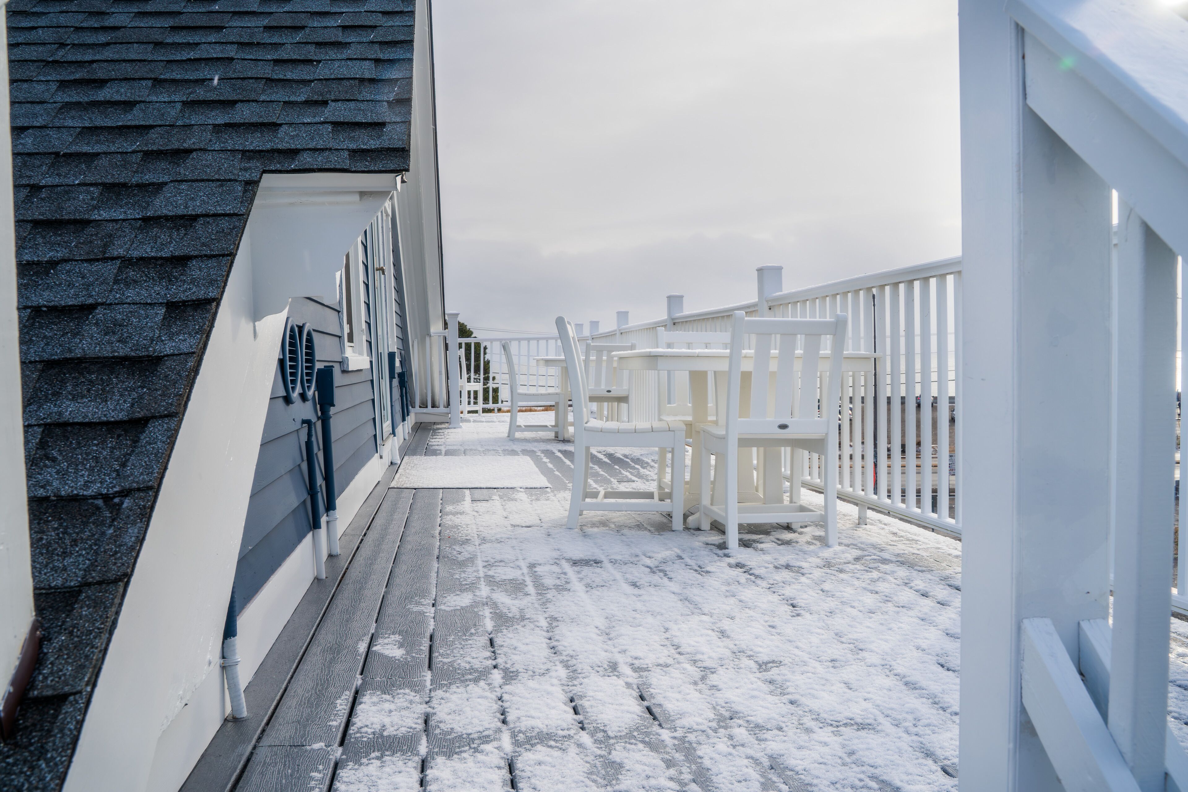 En snötäckt terrass med vita räcken och en mur av tegelsten.