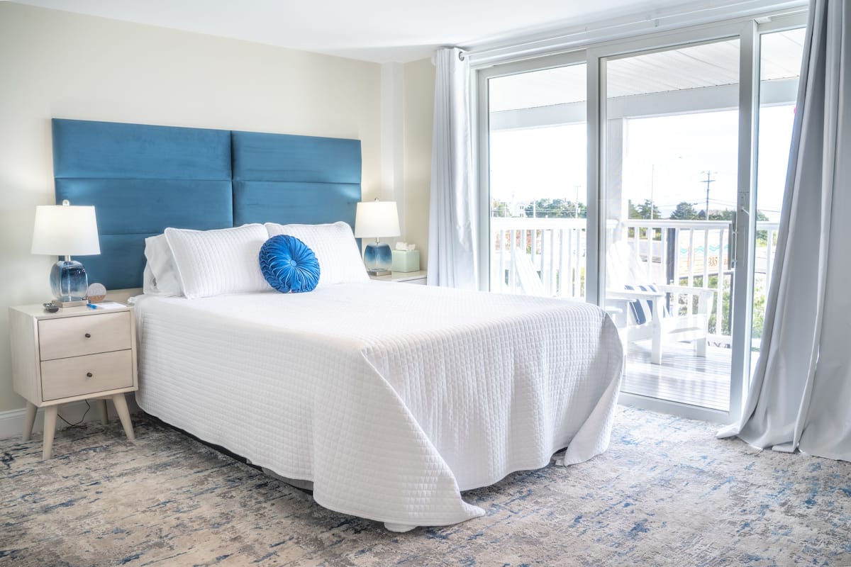 A hotel room with a large bed, two bedside tables with lamps, a view of the balcony through a sliding glass door.