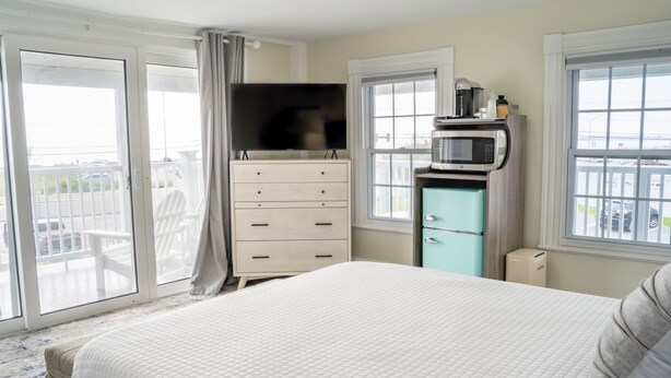 A hotel room with a bed, a dresser, a television, a microwave, and a view of the outside. - 935 Ocean A Beachside Inn (Hampton)