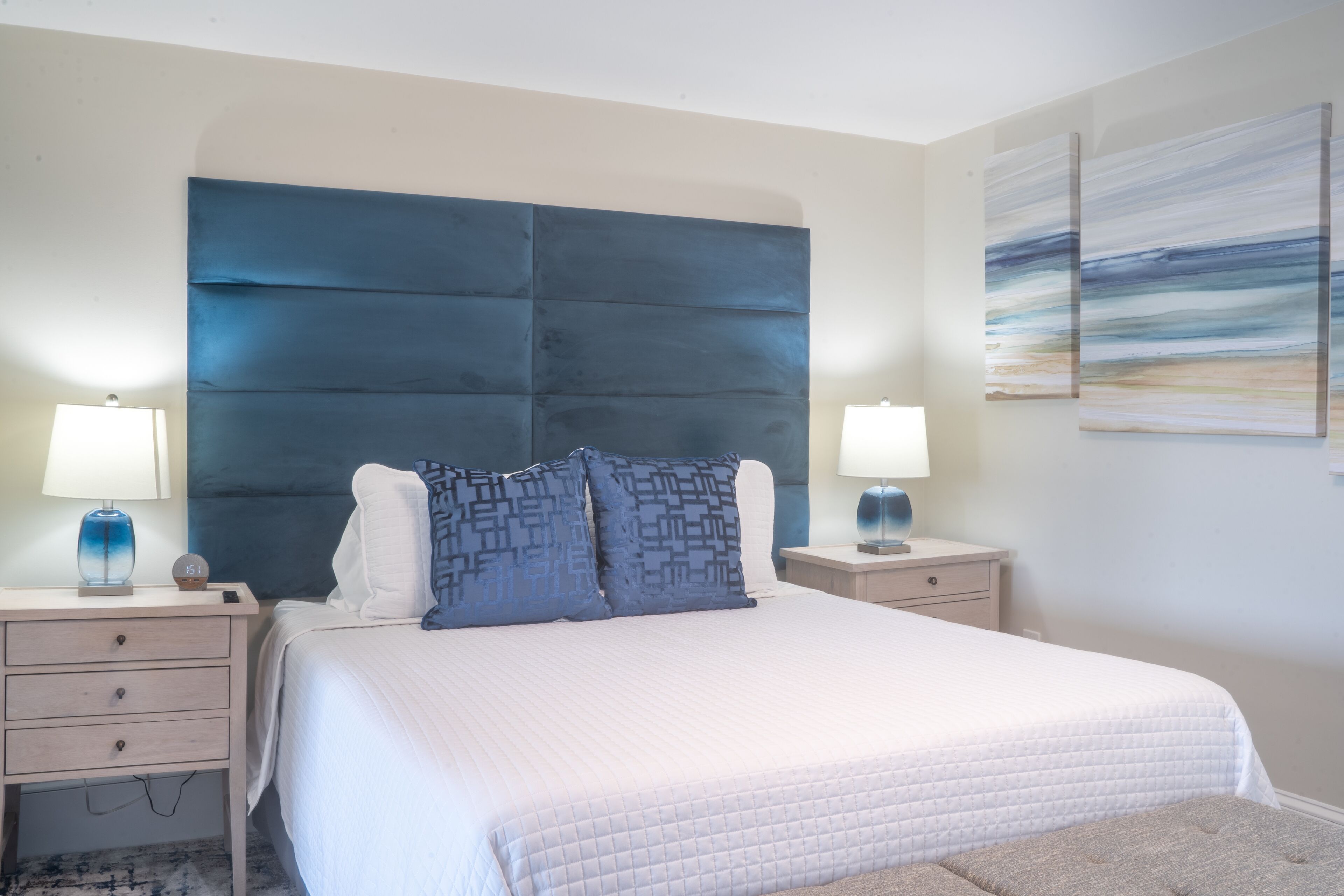 Un dormitorio con una cama grande, dos mesitas de noche, un cabecero y dos lámparas de pared.