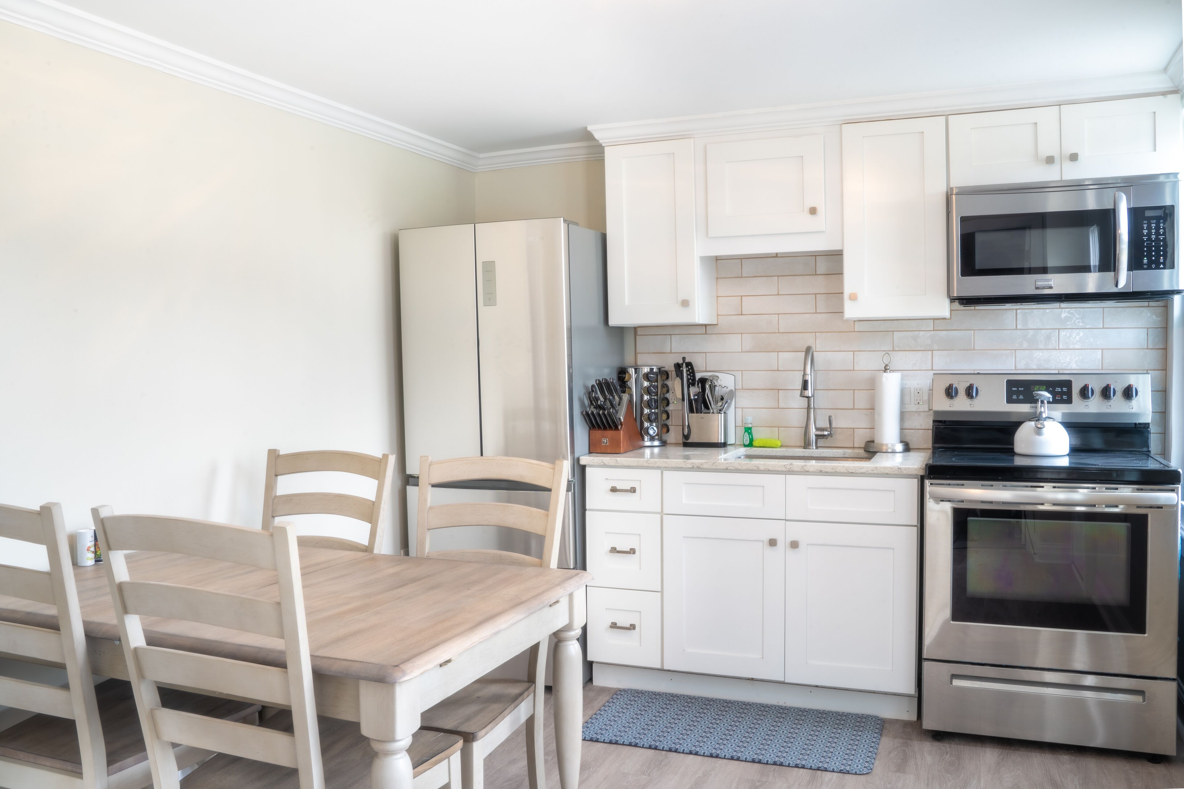 A modern kitchen with white cabinets, stainless steel appliances, and a wooden dining table.