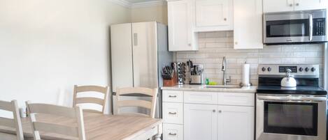 A modern kitchen with white cabinets, stainless steel appliances, and a wooden dining table.