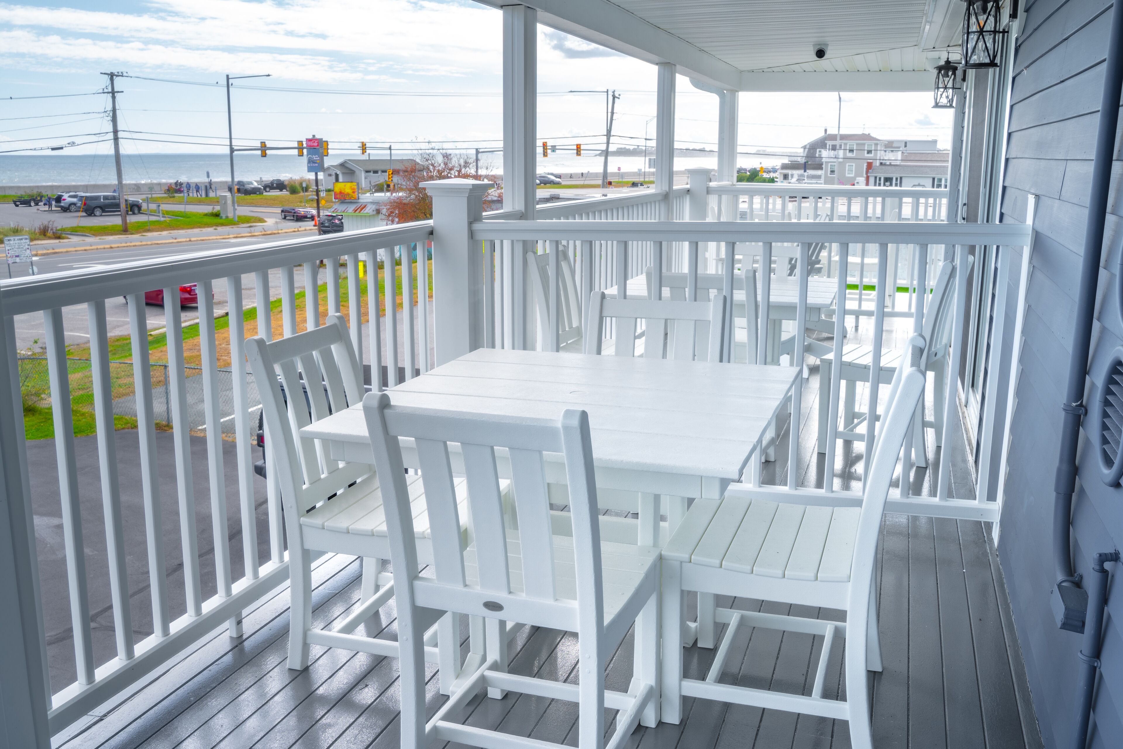 A covered outdoor seating area with white furniture and a view of the street and ocean.