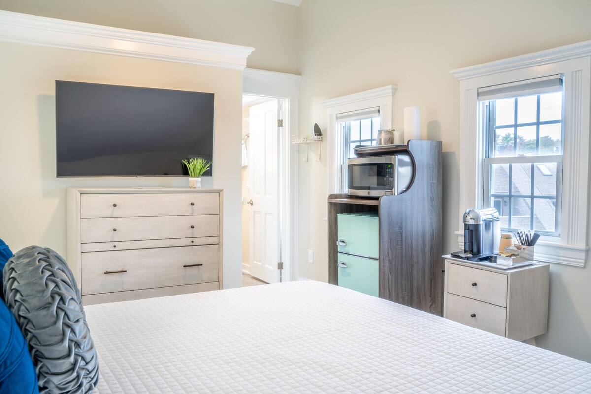 A bedroom with a bed, a dresser, a television, a microwave, and a window.