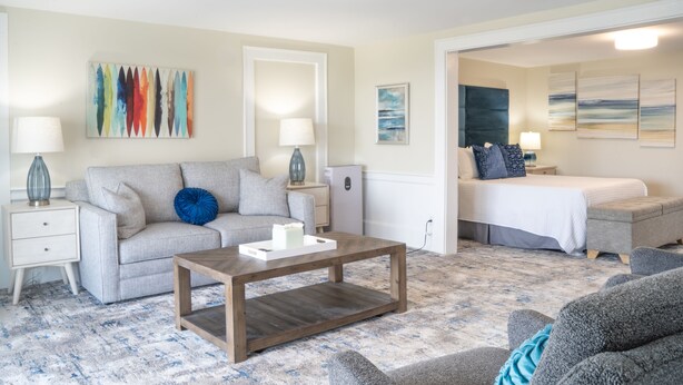 A living room with a sofa, coffee table, and a bed in the background. - 935 Ocean A Beachside Inn (Hampton)
