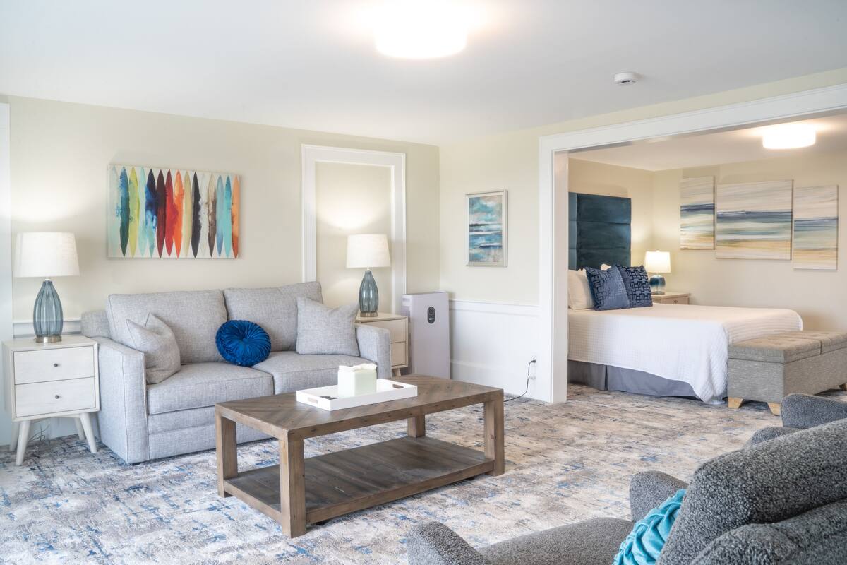 A living room with a sofa, coffee table, and a bed in the background.