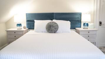 A neatly made bed with a quilted white duvet, a dark blue upholstered headboard, and two bedside tables with lamps and decorative items.