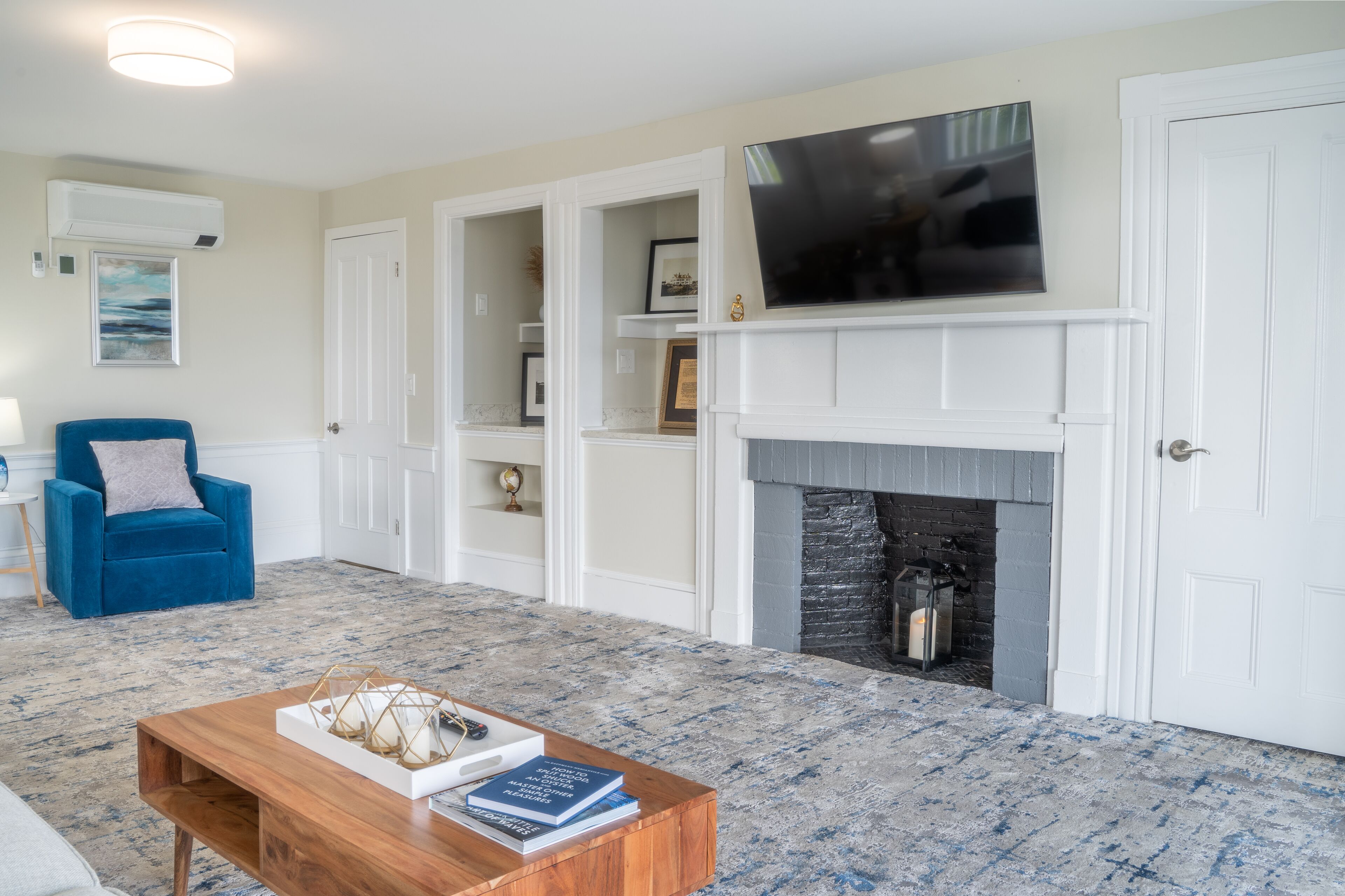 A living room with a fireplace, a blue armchair, a coffee table with books, and a mounted TV.