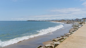 A coastal beach with a concrete walkway and rocky shoreline. - 935 Ocean A Beachside Inn (Hampton)
