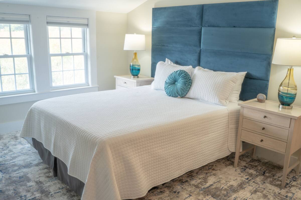 A neatly made bed with a white quilted bedspread, a blue headboard, and two bedside lamps.