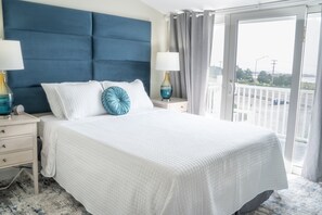 A hotel room with a large bed, two bedside tables, a nightstand, a window with curtains, and a view of the outside.