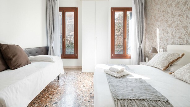 Un dormitorio con dos camas, un papel tapiz estampado y vistas a través de una puerta.