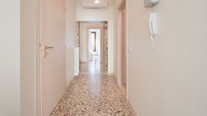 Un pasillo con piso moteado, una puerta a la izquierda y un teléfono a la derecha.