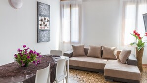 Una sala de estar moderna con un sofá seccional, una mesa de comedor con sillas, un jarrón de flores y un cuadro en la pared.