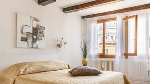 A bedroom with two beds, a large window with a view of a building, a painting on the wall, and a vase with plants. - Accademia Charm 5 by Wonderful Italy (Venecia)