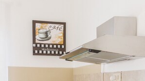 Een compacte keuken met een gasfornuis, een magnetron en een klein spoelbakje. Aan de muur hangt een bord met een welkomstboodschap en op het aanrecht staat een potplant.