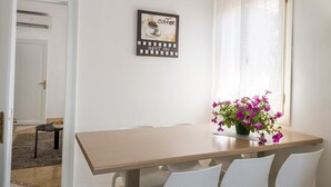 Een eethoek met een houten tafel, witte stoelen, een bord met daarop een koffie-advertentie, en een vaas met roze bloemen.