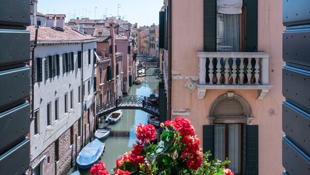 Un canal bordé de bateaux, un bâtiment rose avec des volets et un balcon orné de fleurs.