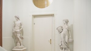 Un pasillo con dos estatuas de mármol, una a cada lado de una puerta blanca.
