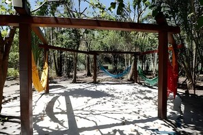 A hammock suspended between wooden posts in a forested area with a dirt path.