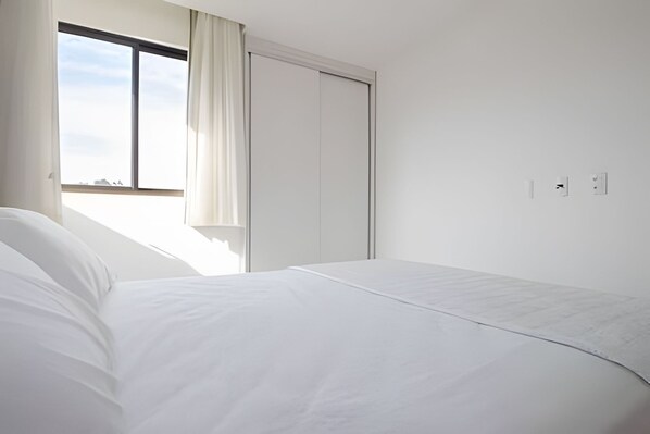 A bedroom with a bed, a window with curtains, a wardrobe, and a wall socket. - Iloa Residence Resort Para 4 Pessoas by MME (Barra de São Miguel)