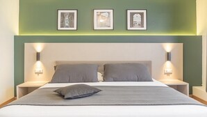 Un lit bien fait, avec deux oreillers et une couverture, flanqué de deux tables de chevet sur lesquelles sont posées des lampes murales. Au-dessus du lit, on peut voir trois tableaux encadrés accrochés au mur.