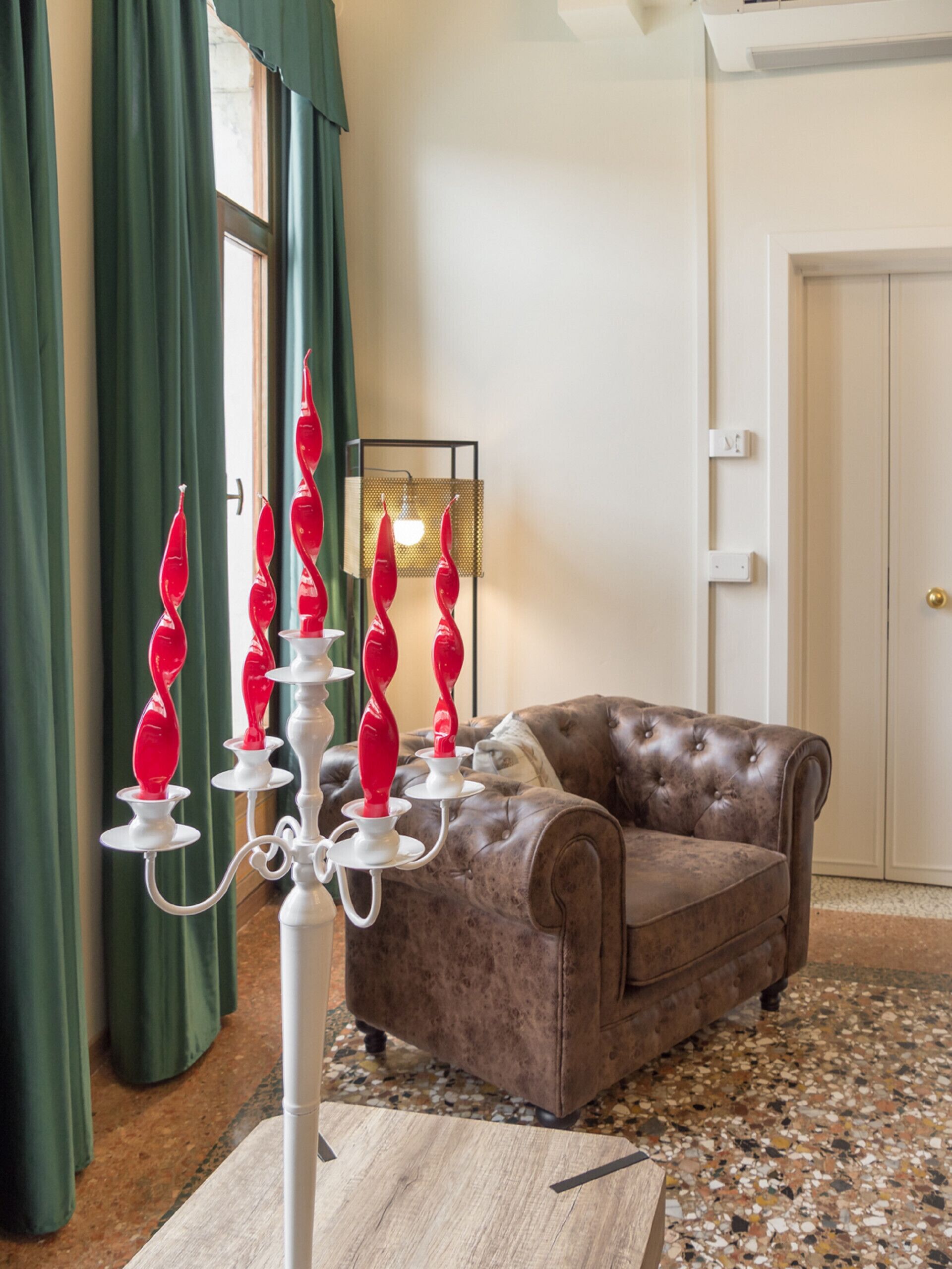 Ein Zimmer mit einem braunen Ledersofa, einer weißen Stehlampe mit roten Kerzen und einem grünen Vorhang.