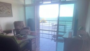 A living room with a view of the sea, furnished with a sofa, chairs, and a table. - Quiet Beach Front Condo with patio overlooking Infinity Pool & Ocean (Puerto Morelos)