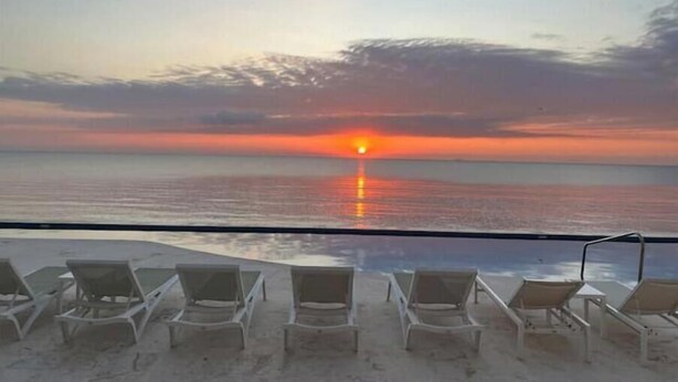 A beach view with lounge chairs facing the ocean at sunset. - Quiet Beach Front Condo with patio overlooking Infinity Pool & Ocean (Puerto Morelos)