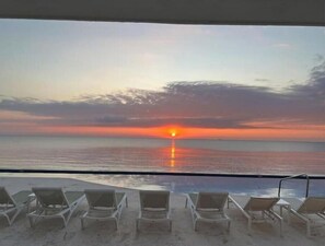 Een uitzicht op het strand met ligbedden gericht op de oceaan bij zonsondergang.