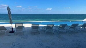 A beach with lounge chairs and a pool. - Quiet Beach Front Condo with patio overlooking Infinity Pool & Ocean (Puerto Morelos)